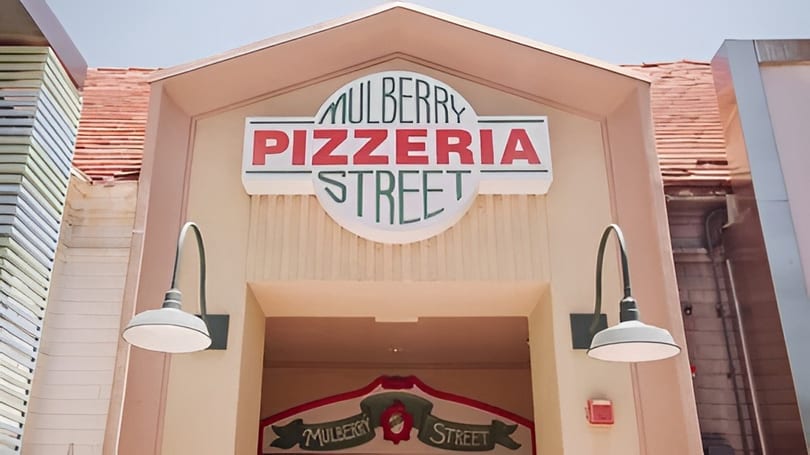 Mulberry Pizzeria Street sign on a light-colored building with two outdoor lamps and a red roof.