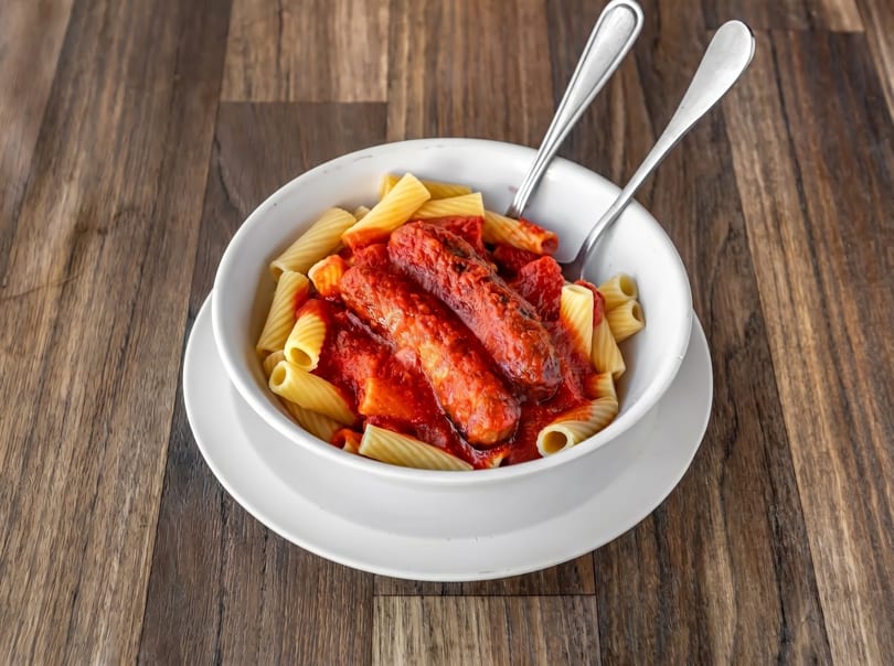 Rigatoni pasta with two sausages in red marinara sauce, served in a white bowl with forks.