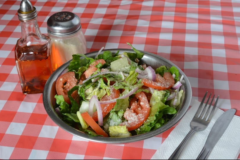 Fresh garden salad with lettuce, tomatoes, onions, and cheese on a red and white checkered tablecloth.